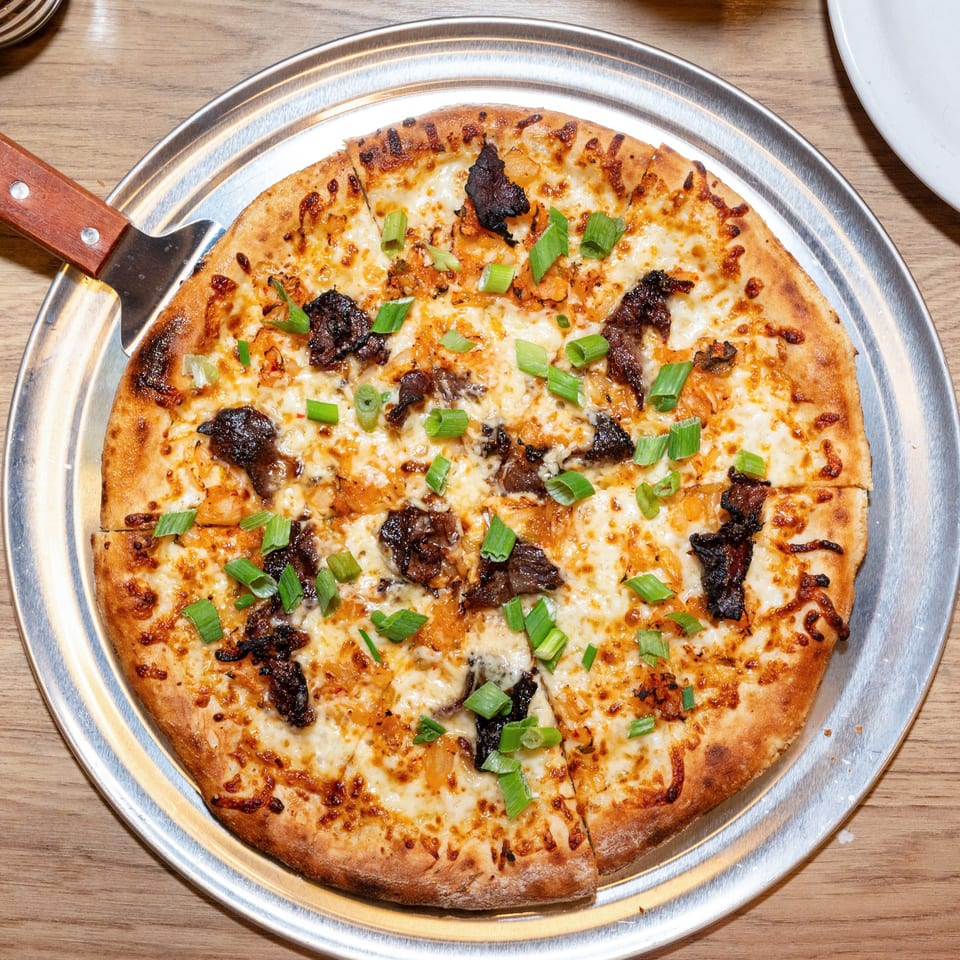 A whole pizza with white cheese, dark meat, and green onions on a metal tray.