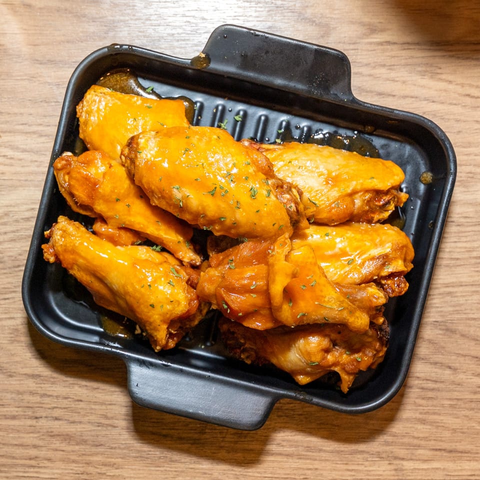 A black rectangular dish filled with golden-brown chicken wings coated in a glossy orange sauce.