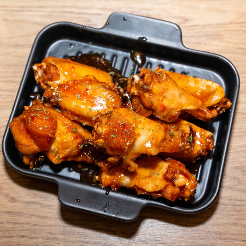 Sweet and spicy Korean fried chicken wings, garnished with herbs, served in a black tray.