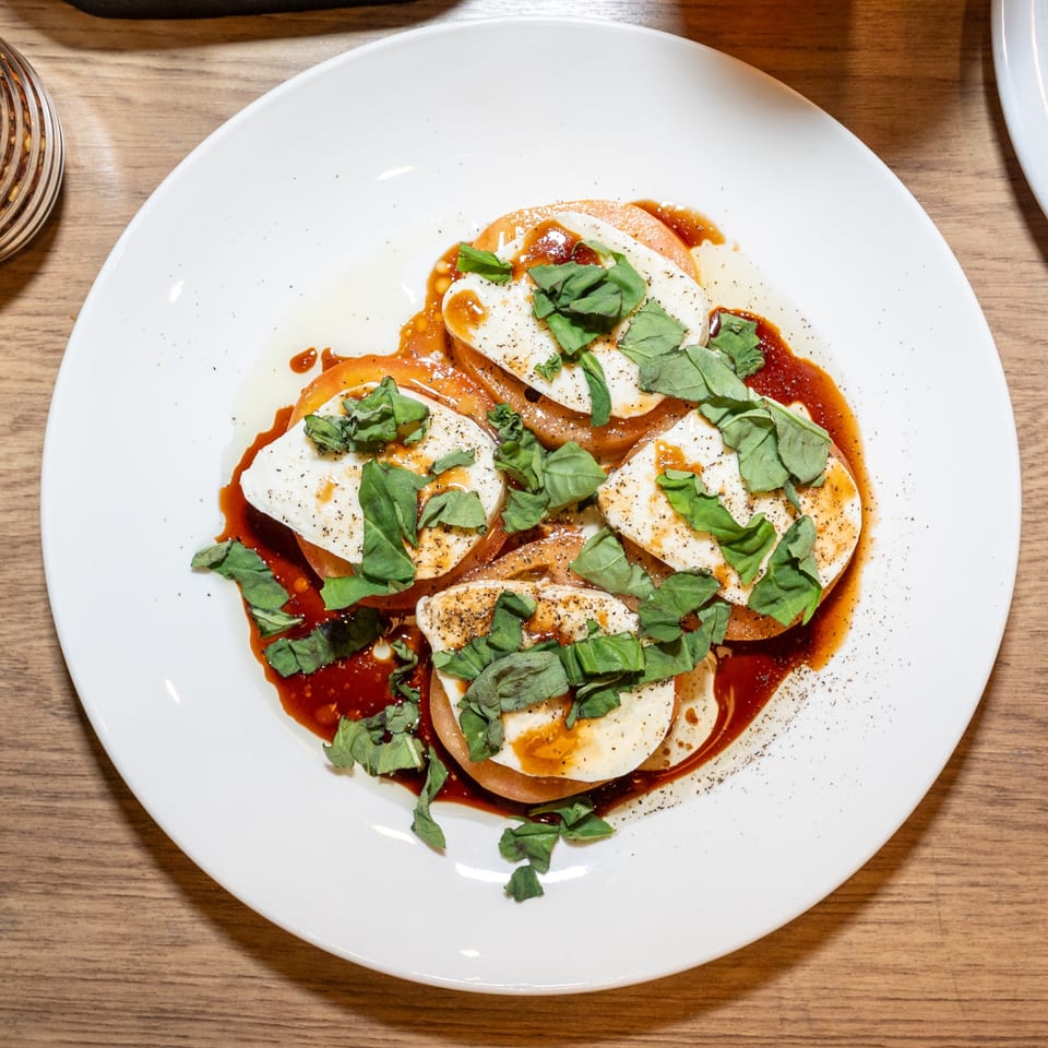Caprese salad with sliced tomatoes, fresh mozzarella, basil, balsamic glaze, and pepper on a white plate.