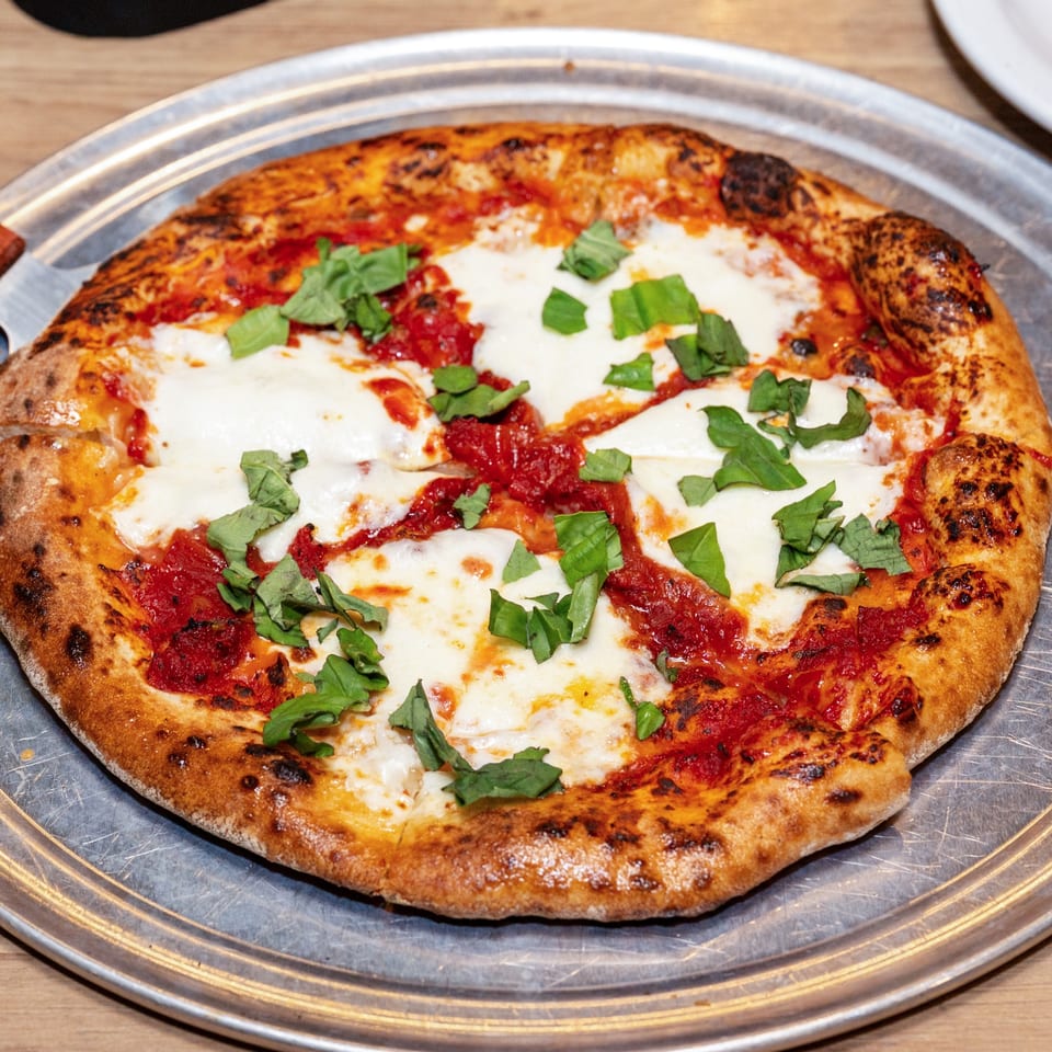 A freshly baked Margherita pizza with melted mozzarella, red sauce, and basil on a metal tray.